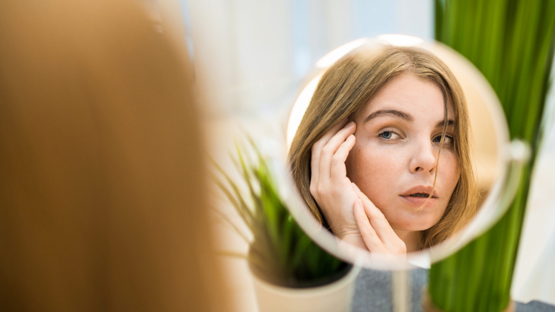 A young caucasian woman is looking in the mirror and posing